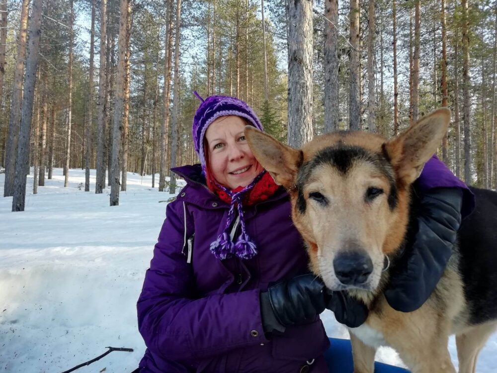 Mervi Valjus ja koira lumisessa metsässä. for 